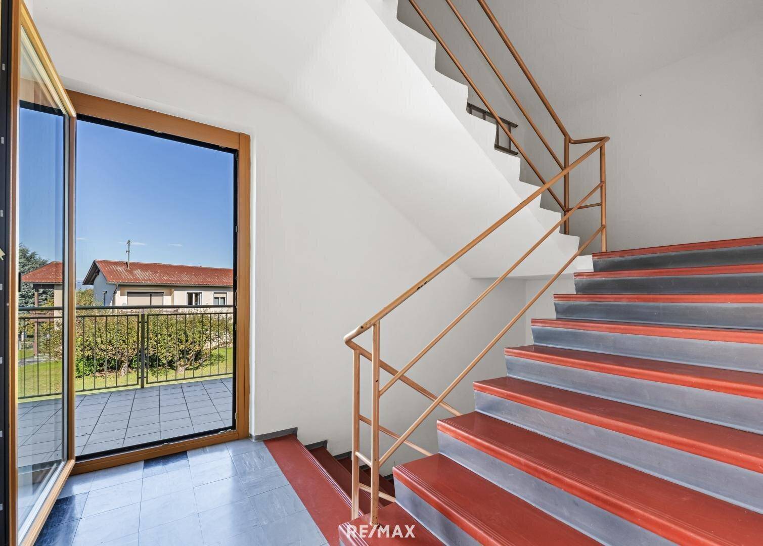 Treppenhaus mit Zugang zu einer Terrasse und großen Fenstern, die viel Licht hereinlassen.