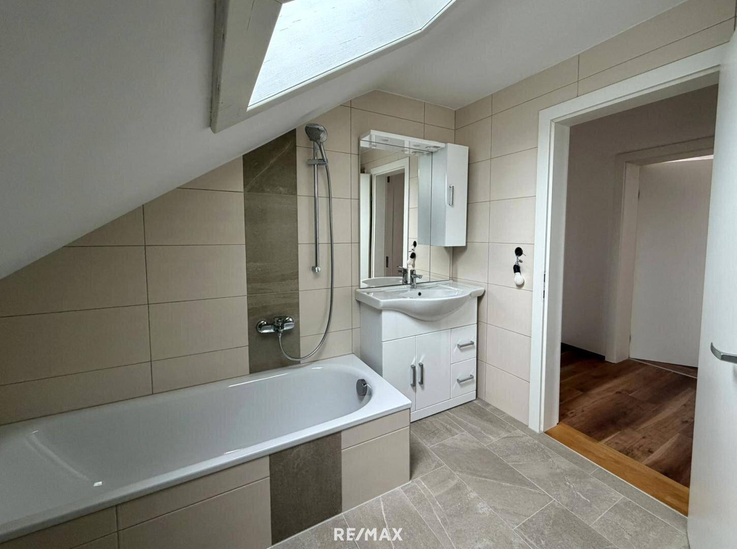 Badezimmer im Dachgeschoss mit Badewanne, Waschbecken, Spiegelschrank und Fliesenboden.