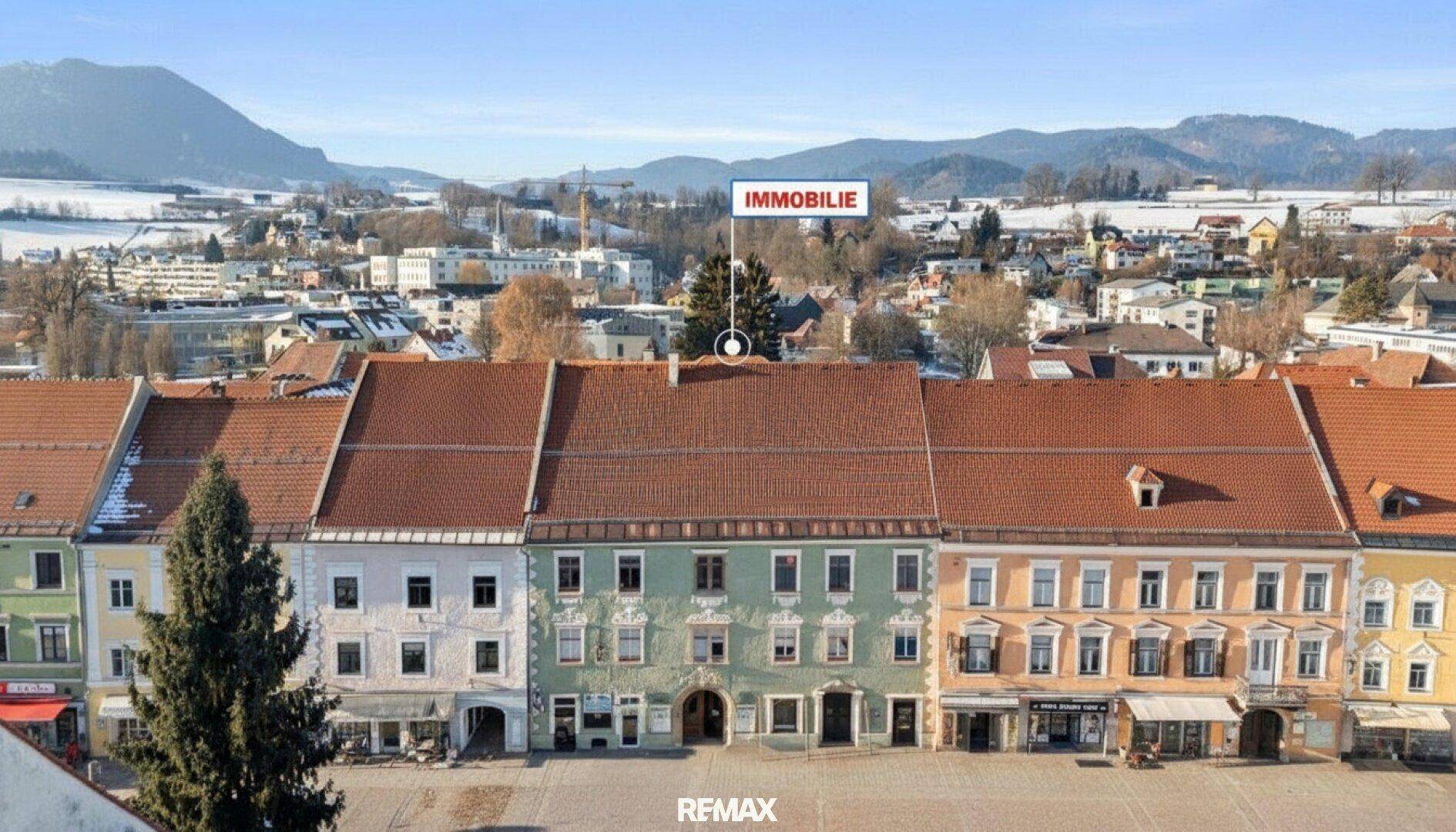 Luftaufnahme der Stadt mit markiertem Gebäude und schneebedeckten Bergen im Hintergrund.