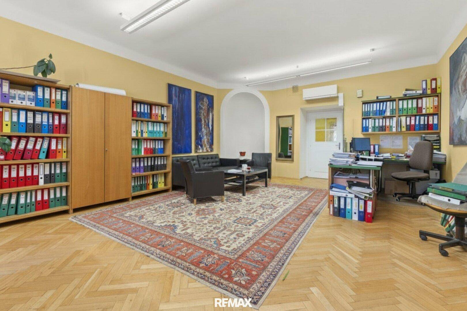 Weitläufiges Büro mit Fischgrätparkett, Aktenregalen und einem Teppich als zentrales Element.