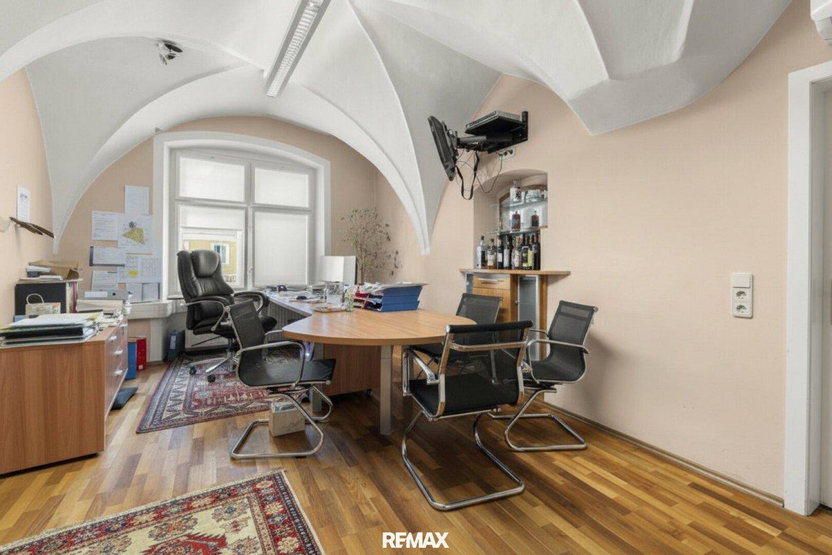 Helles Büro mit Holzboden, Gewölbedecke und großem Schreibtischbereich.