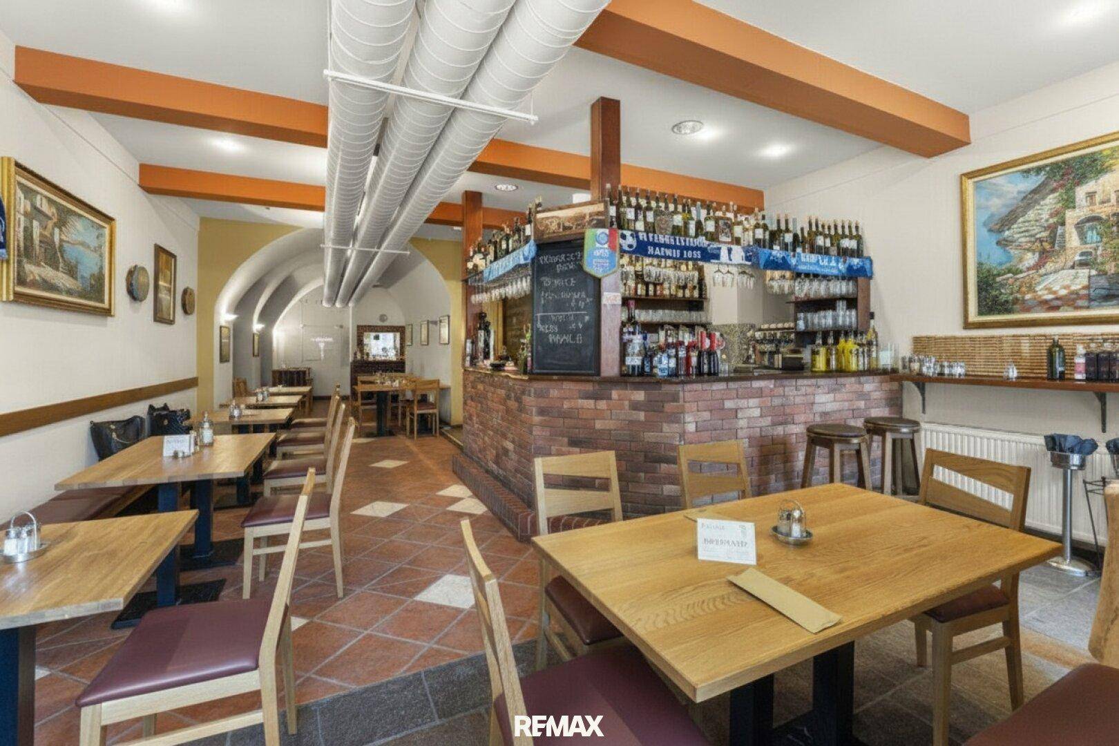 Gemütlicher Restaurantbereich mit Bar, Holztischen und Terrakotta-Fliesenboden.
