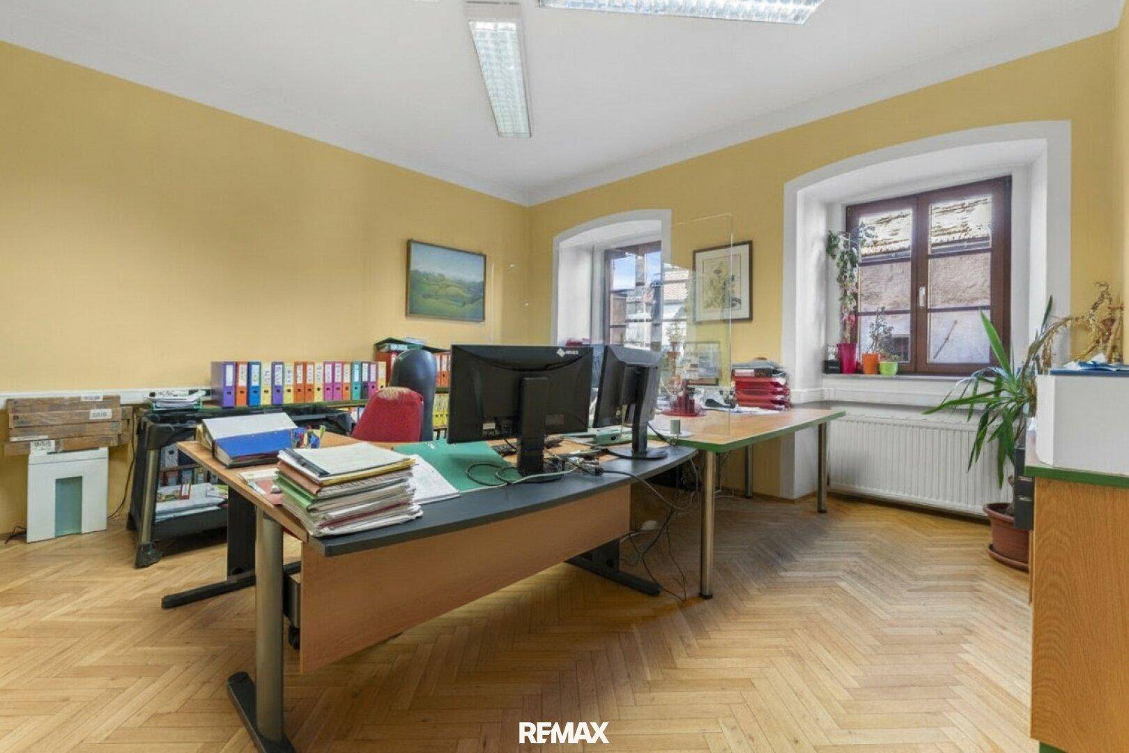 Geräumiges Büro mit Fischgrätparkett und zwei Fenstern, hell und funktional eingerichtet.