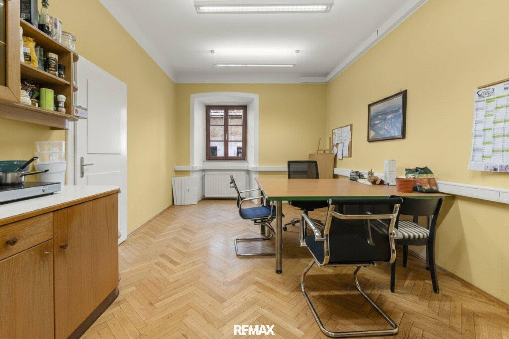 Büro mit Holzboden, kleinem Küchenbereich und Besprechungstisch.