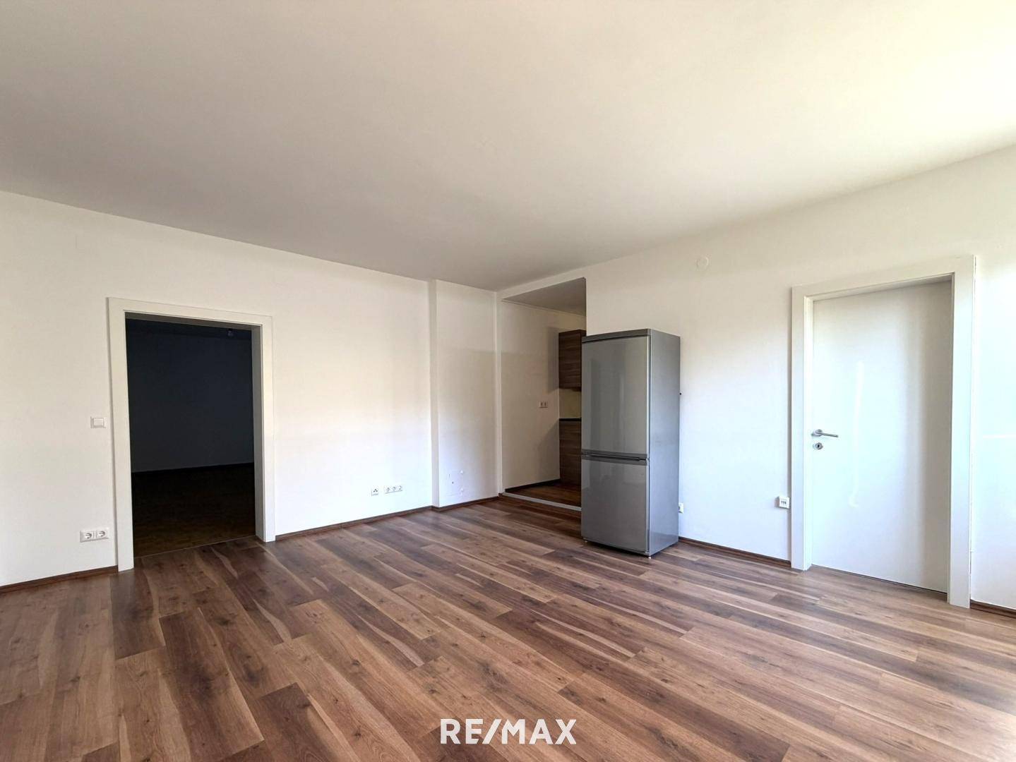 Heller Wohnbereich mit Laminatboden und einem Kühlschrank, angrenzend an eine Küchennische.