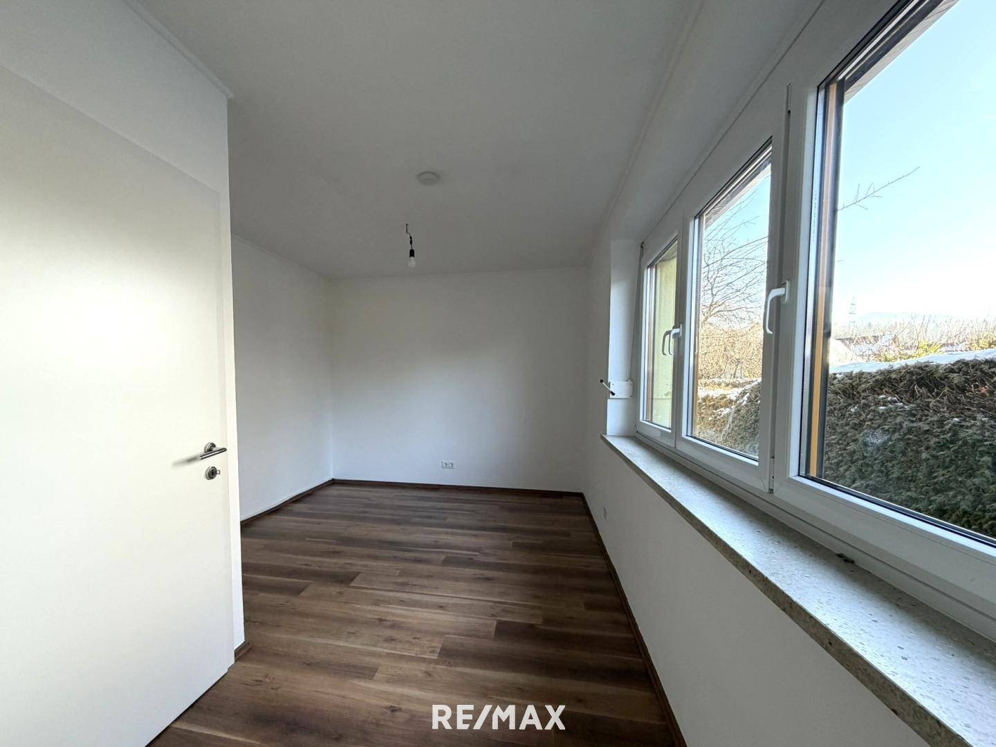 Helles Schlafzimmer mit Laminatboden und großen Fenstern, die viel Tageslicht hereinlassen.