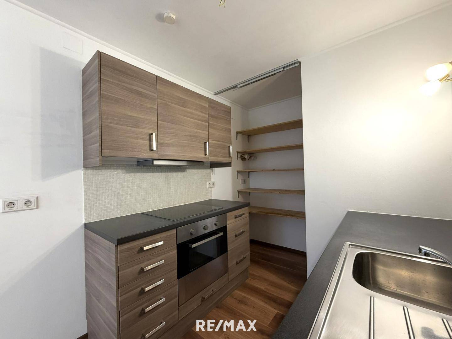 Funktionale Küchenzeile mit Holzschränken, Kochfeld und integriertem Backofen, inklusive Speisekammer.