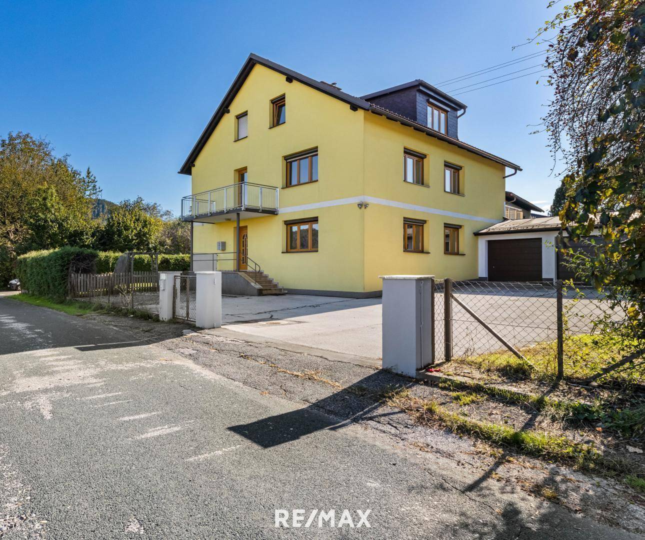 Gelbes Einfamilienhaus mit Balkon und Garage, umgeben von einem gepflegten Grundstück.