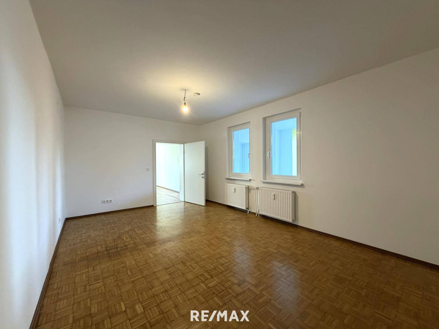 Geräumiger, heller Raum mit Parkettboden und zwei Fenstern, ideal als Wohn- oder Schlafzimmer.