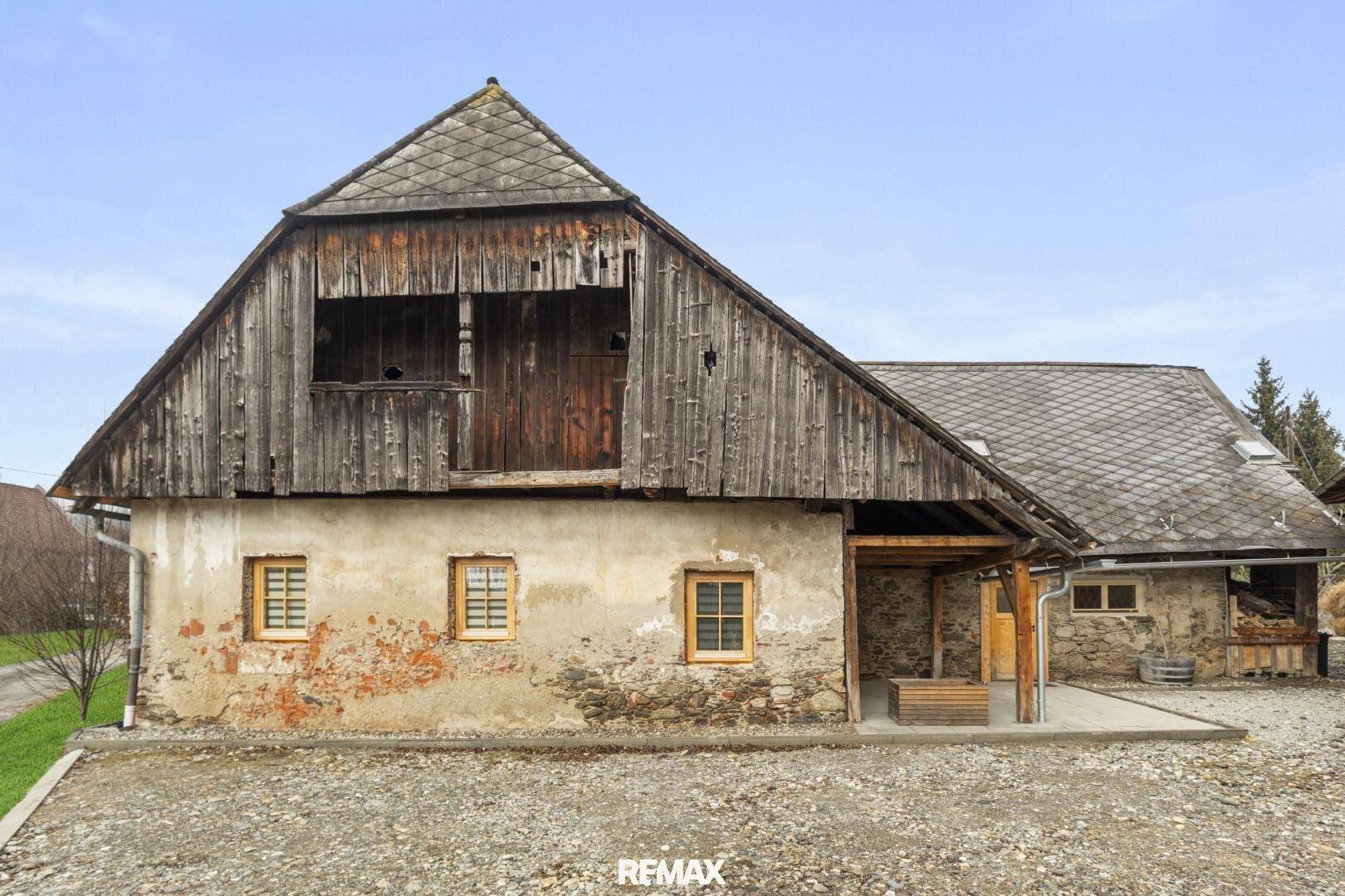Historisches Bauernhaus mit rustikaler Fassade, Holzbalkon und angrenzendem Schuppen.