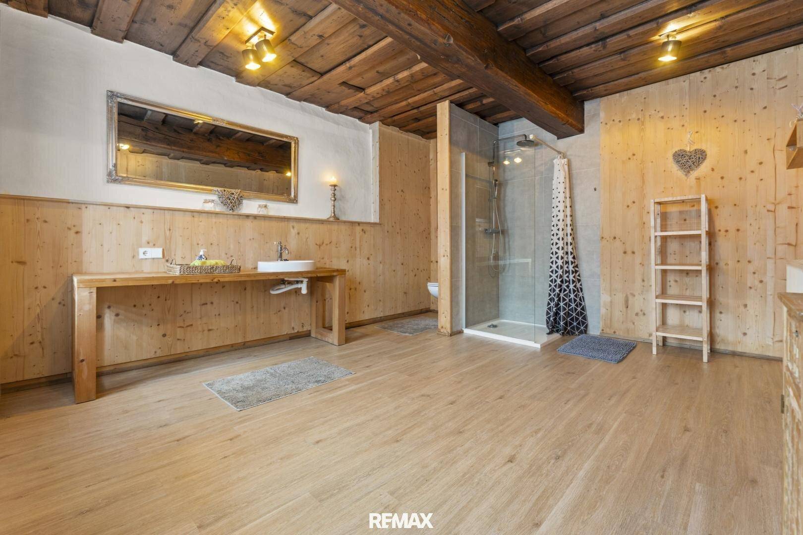 Rustikales Badezimmer mit Holzwänden, Holzbalkendecke, Einzelwaschbecken und Duschkabine.