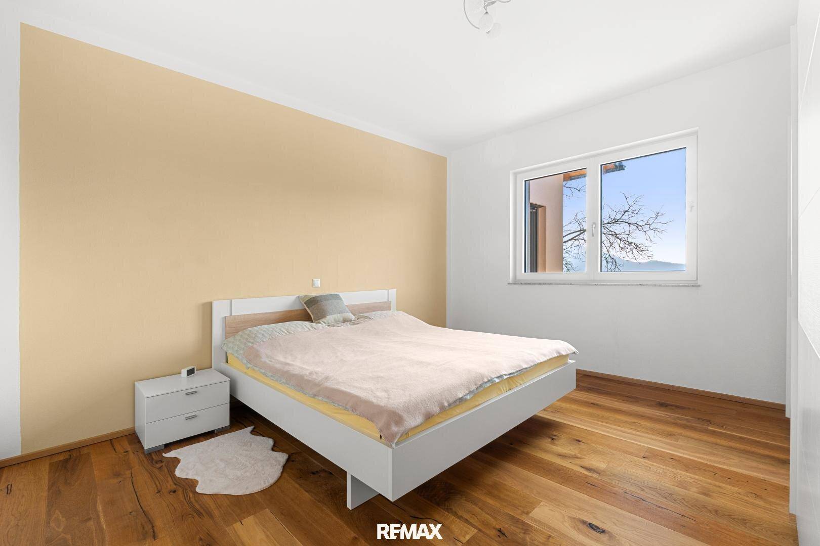 Helles Schlafzimmer mit Holzboden, einem Doppelbett, Nachttisch und einem Fenster mit Blick ins Grüne.