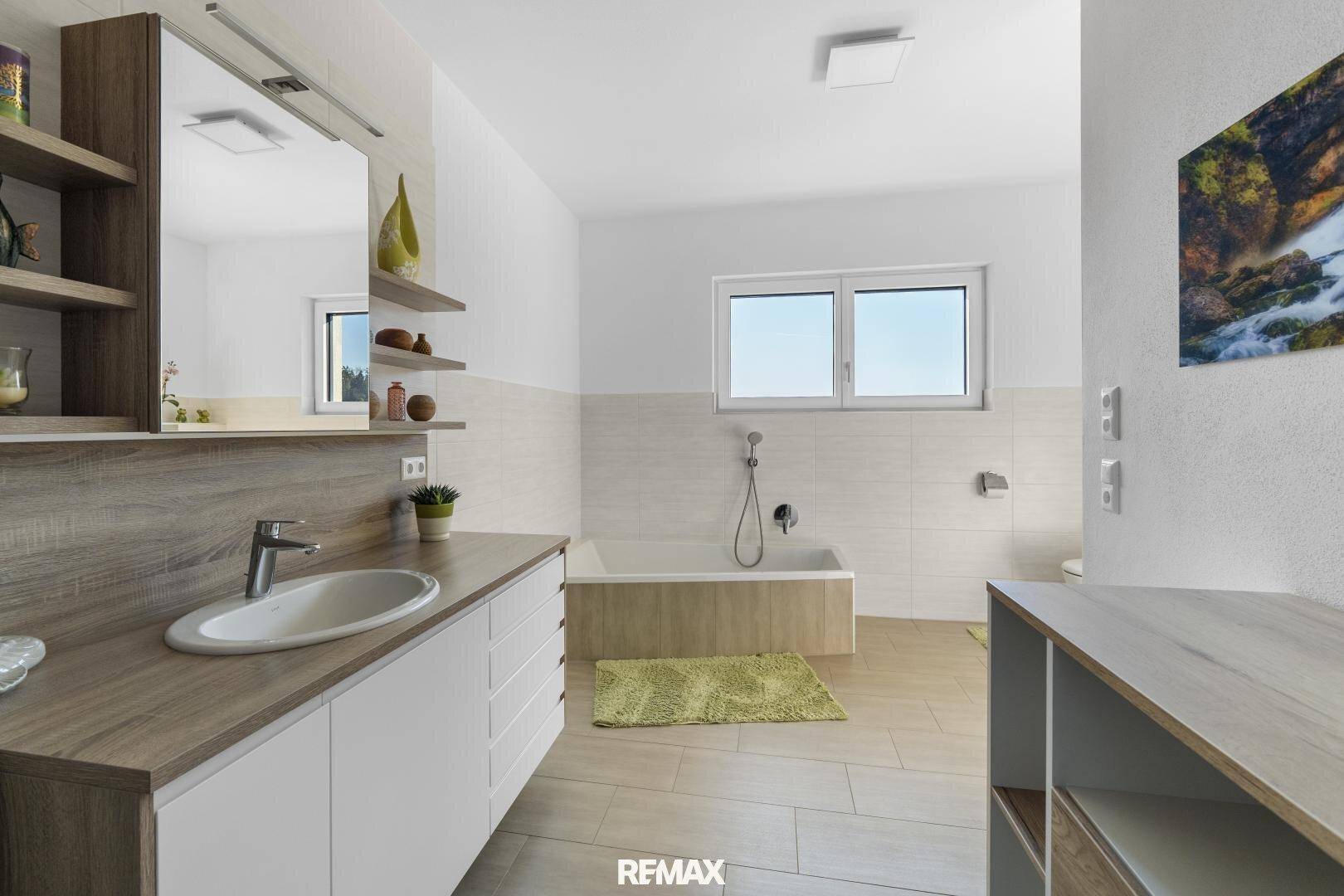 Helles Badezimmer mit Holzoptik-Waschtisch, Badewanne und Fenster für natürliche Belichtung.