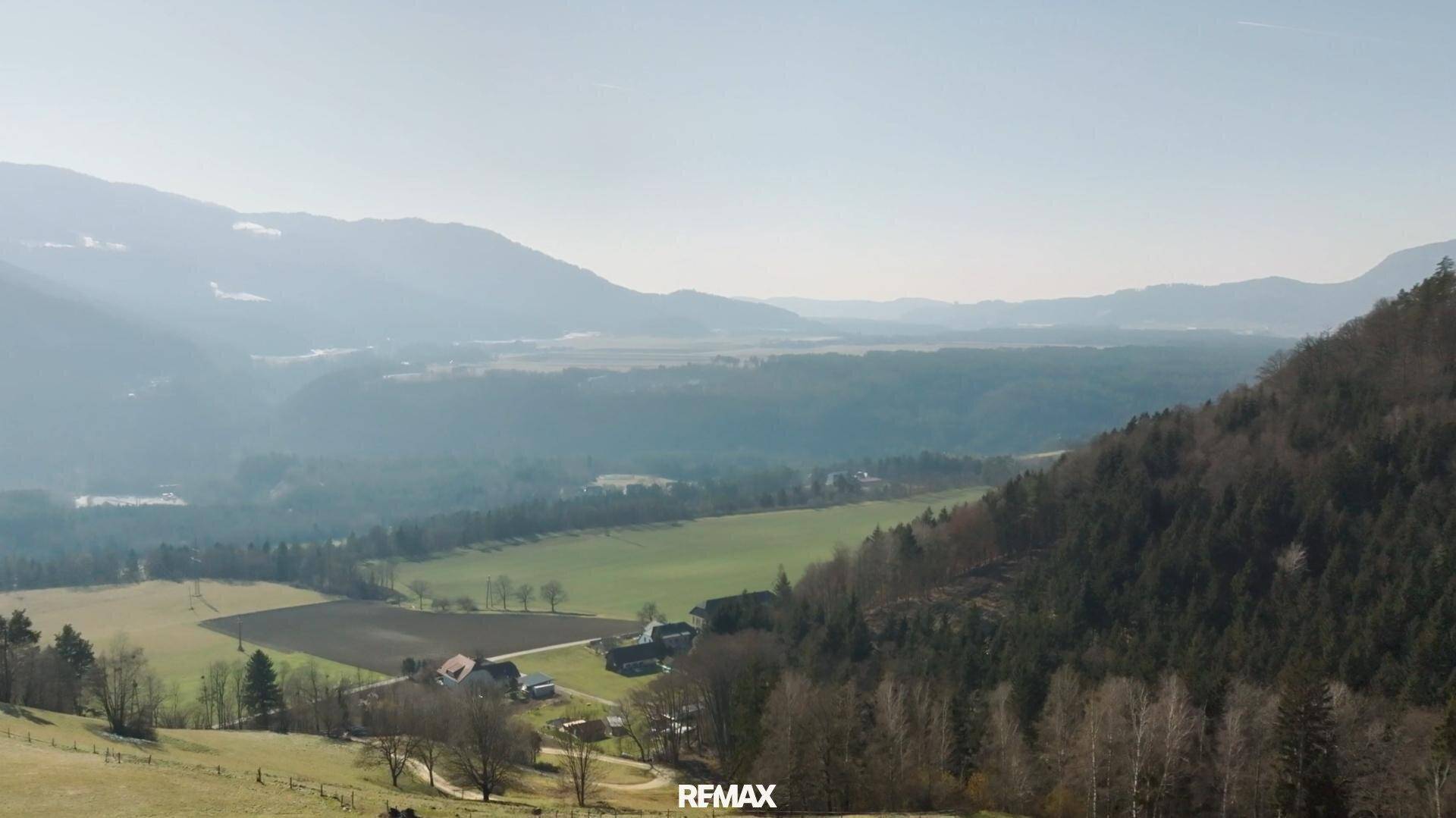 Weitläufiger Blick über ein Tal mit Feldern, Wäldern und Bergen unter einem klaren Himmel.