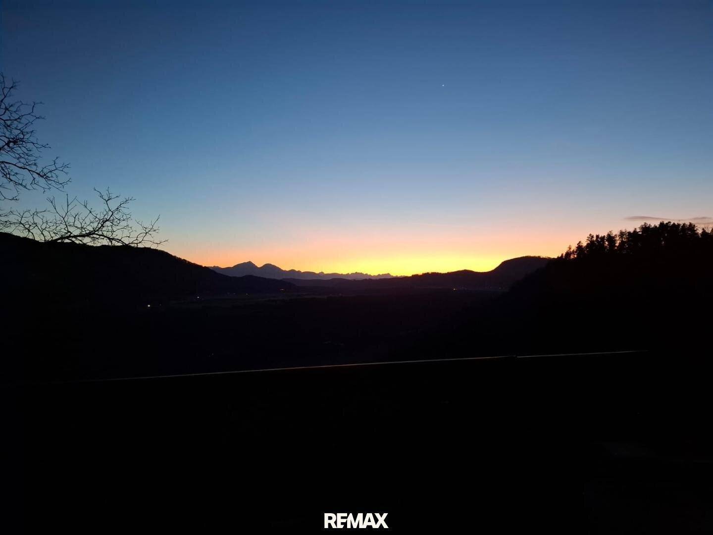 Weitläufiger Blick auf den Sonnenuntergang über einer Berglandschaft mit dunklem Vordergrund.