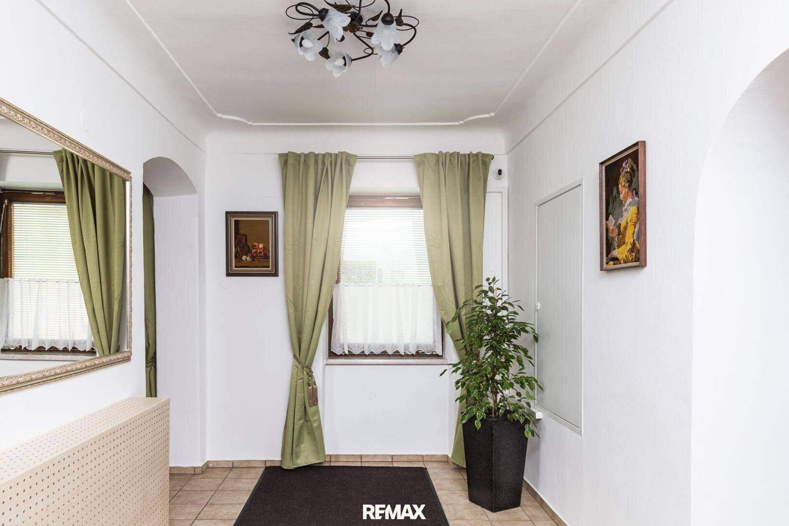 Heller Flur mit Fliesenboden, grünen Vorhängen und einem großen Spiegel.