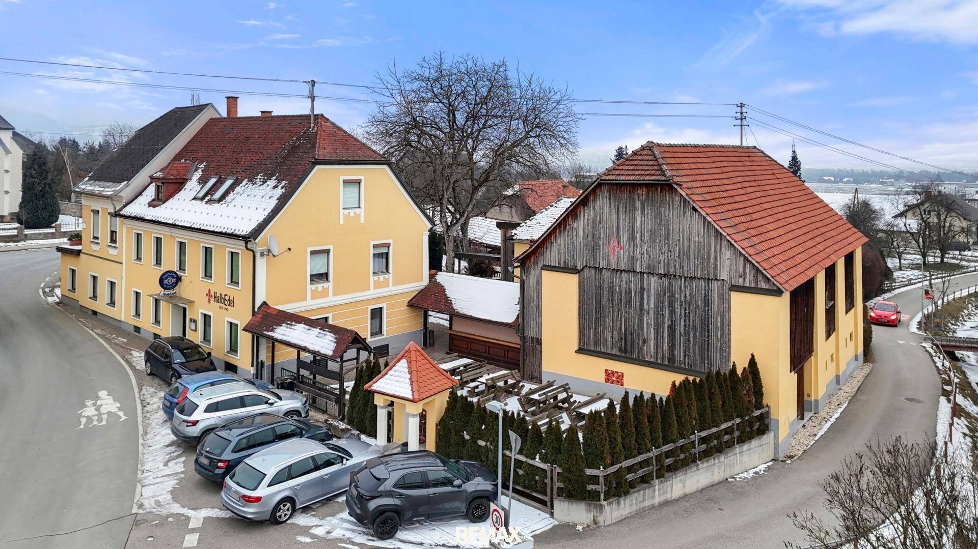 Luftaufnahme des Anwesens mit gelbem Hauptgebäude, Scheune und verschneiter Landschaft.