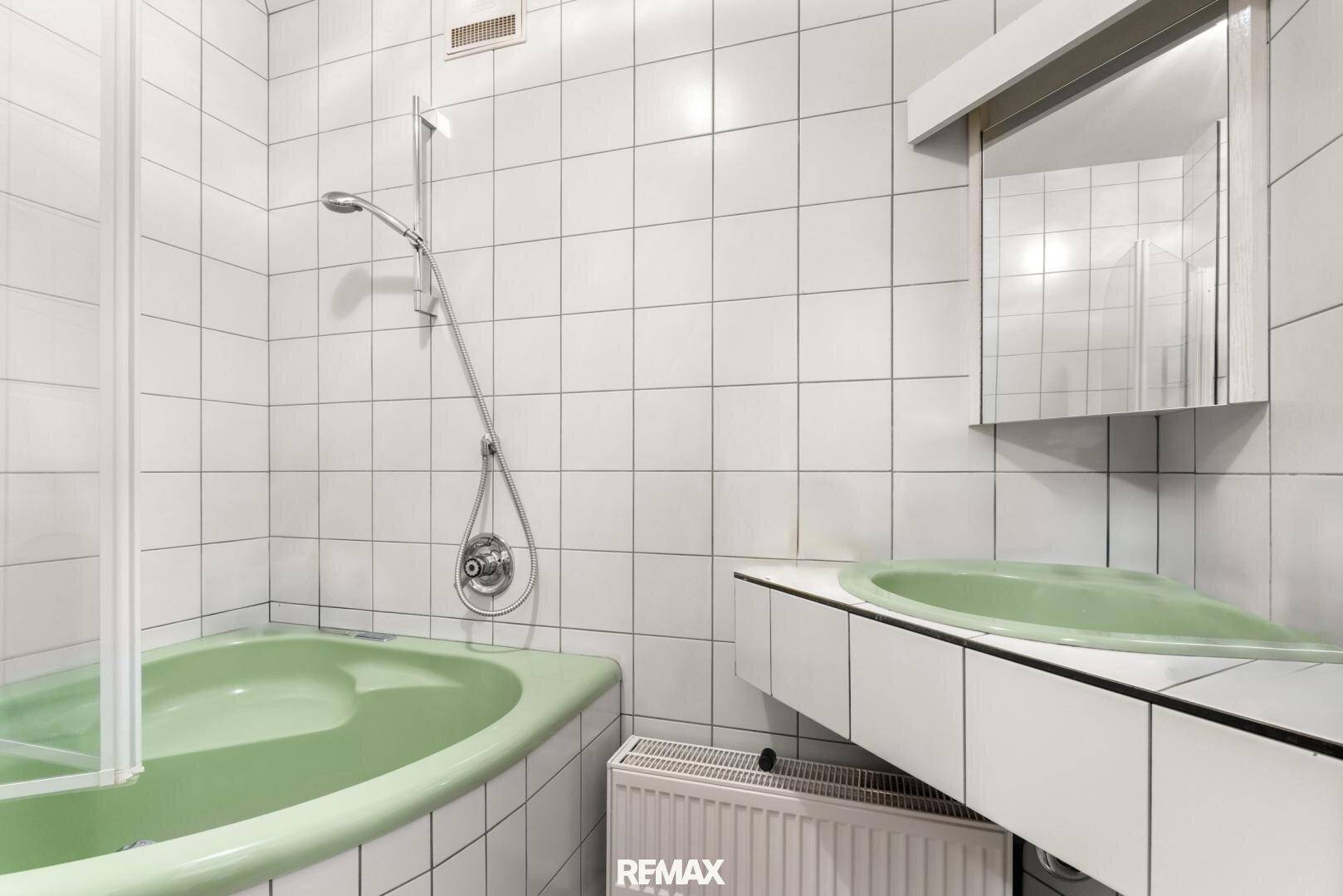 Badezimmer mit grüner Badewanne, Waschbecken und weißen Fliesen an den Wänden.