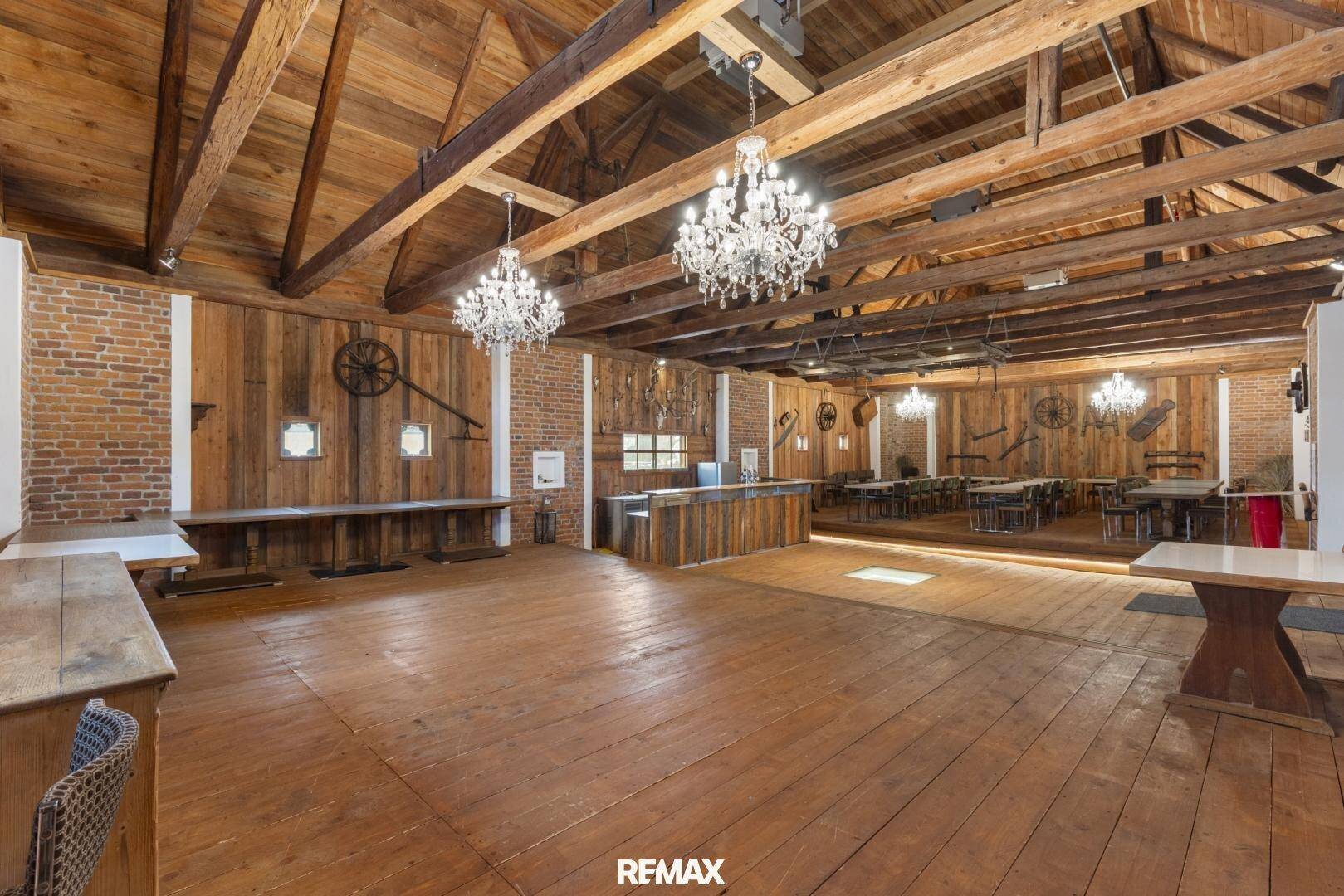 Großer Veranstaltungssaal mit Holzboden, Holzbalkendecke und rustikaler Bar.