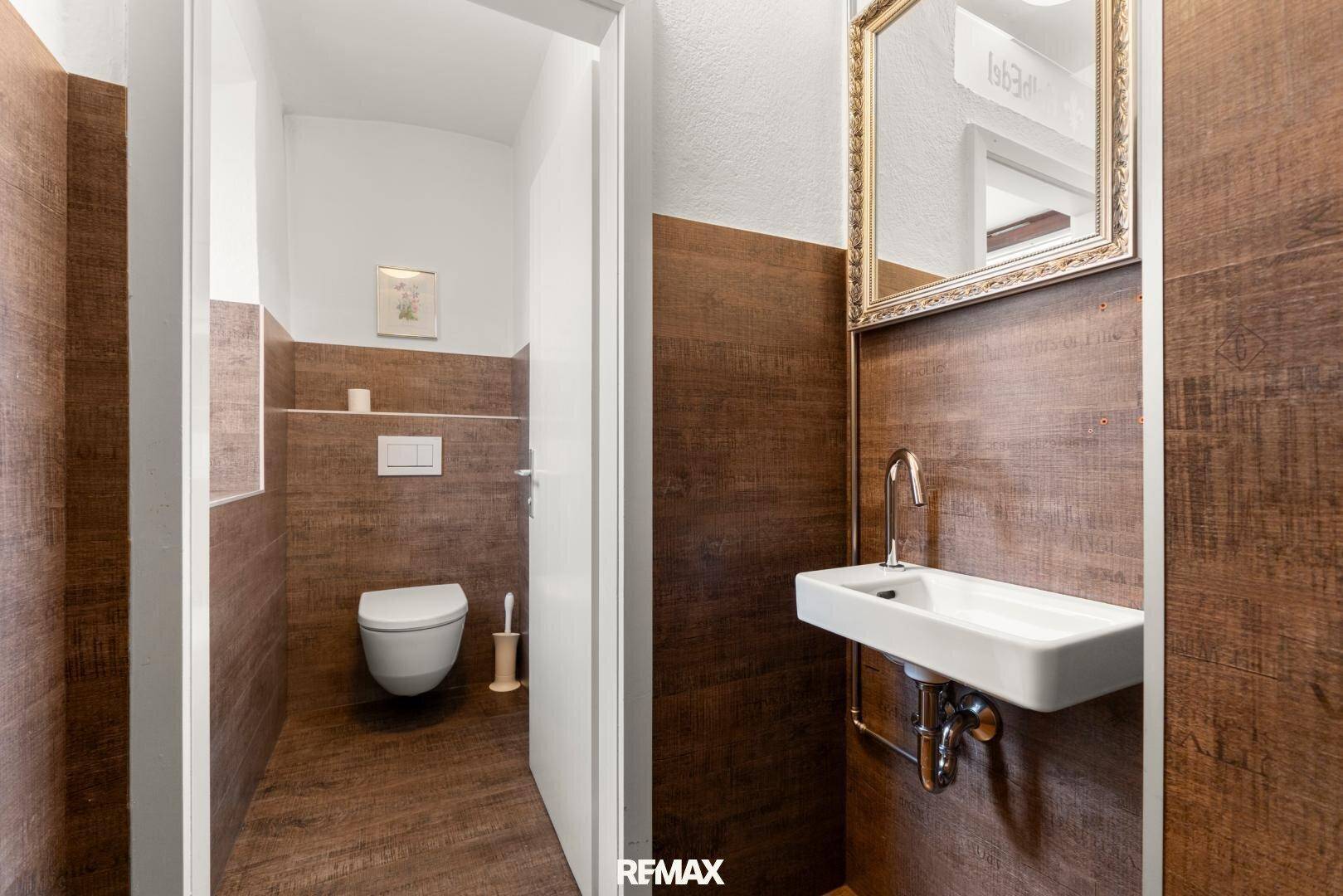 Moderne Gästetoilette mit Holzwandverkleidung, wandmontierter Toilette und kleinem Waschbecken.