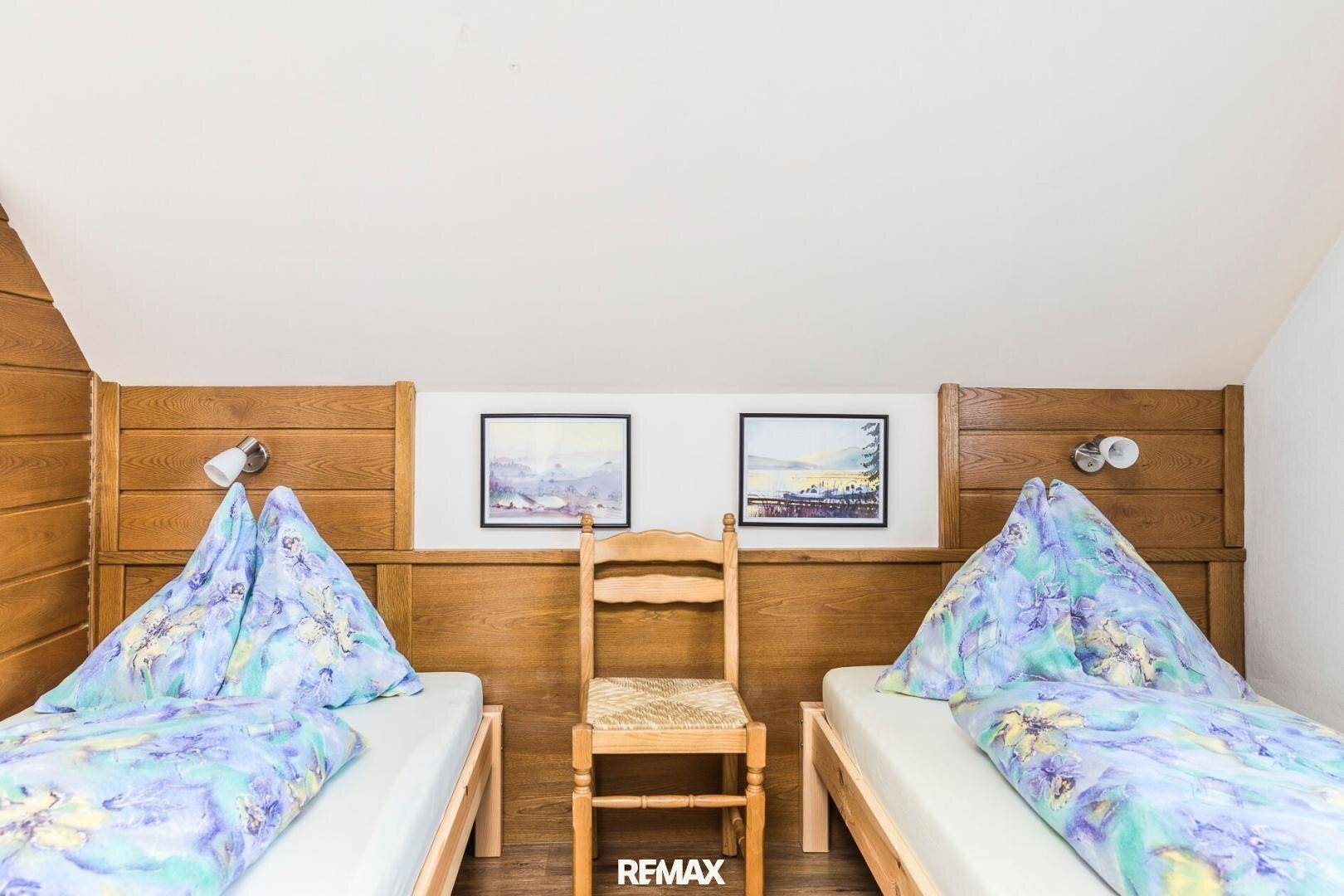 Gemütliches Schlafzimmer im Dachgeschoss mit Holzwandverkleidung, zwei Einzelbetten und Dachschräge.