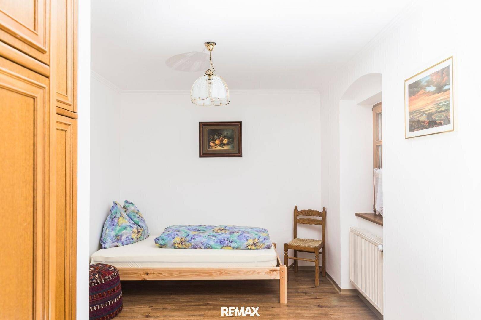Einfaches Schlafzimmer mit Einzelbett, Holzschrank und Fenster mit Blick nach draußen.