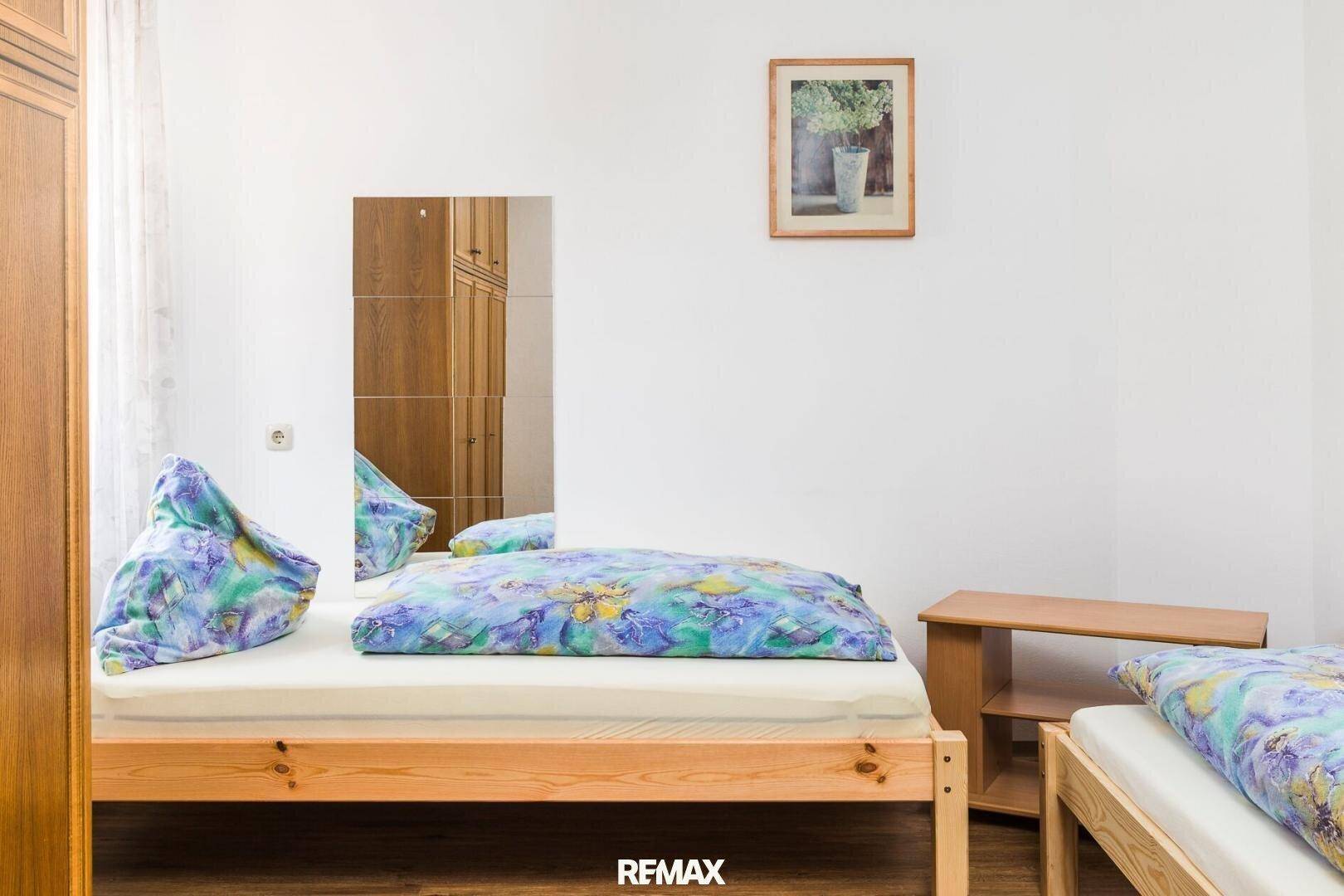 Helles Schlafzimmer mit zwei Einzelbetten, Holzschrank und einfacher, funktionaler Einrichtung.