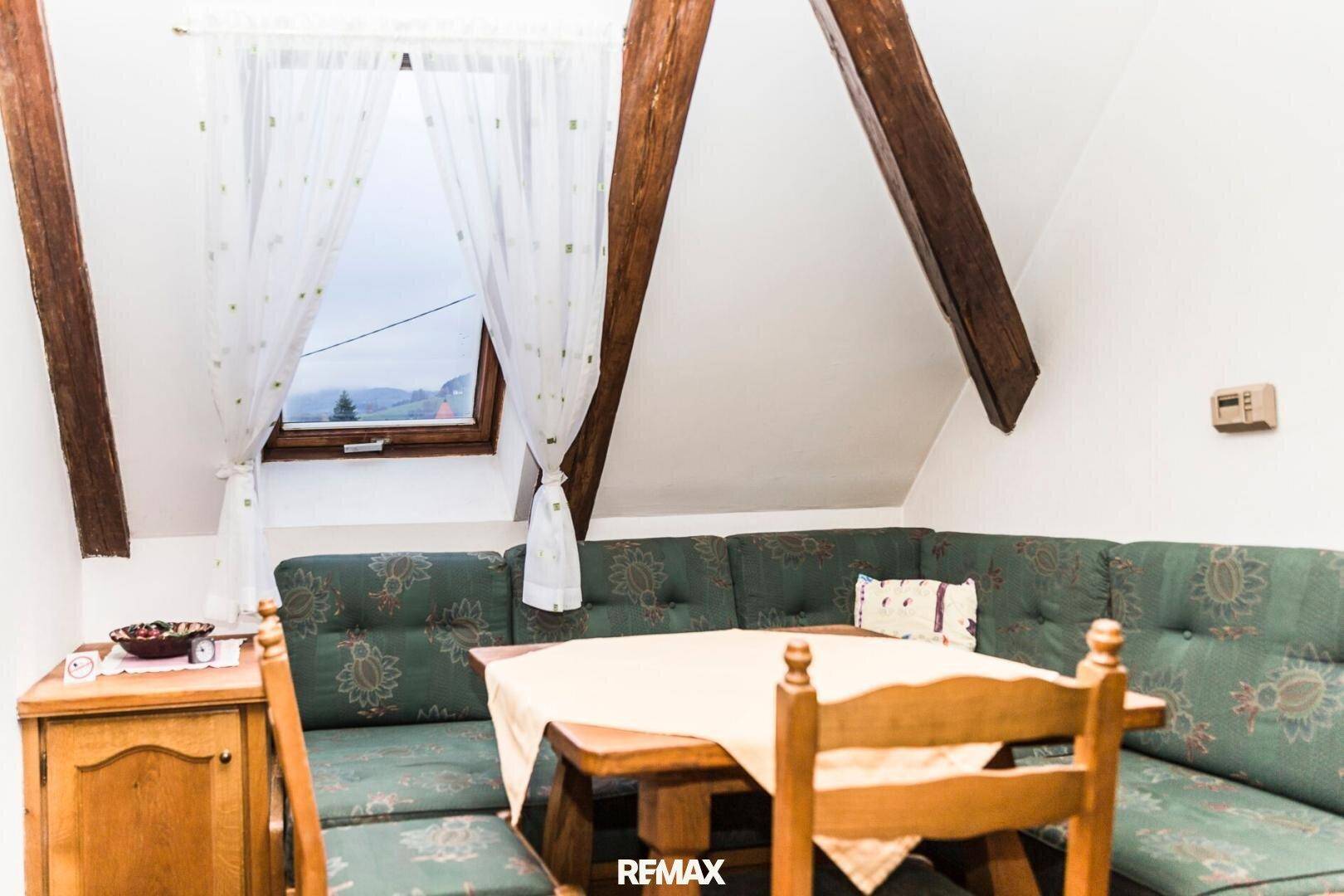 Dachgeschoss-Wohnzimmer mit sichtbaren Holzbalken, gemütlicher Sitzecke und Dachfenster.