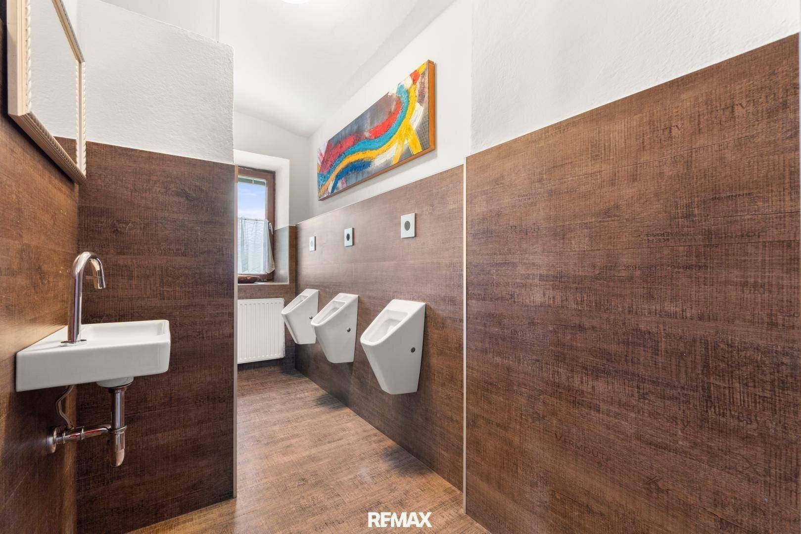 Öffentliche Herrentoilette mit Urinalen, Holzwandverkleidung und modernem Waschbecken.