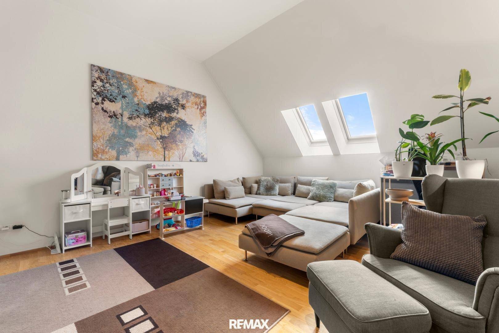 Gemütliches Wohnzimmer im Dachgeschoss mit großem Sofa, Teppich und Dachfenstern.
