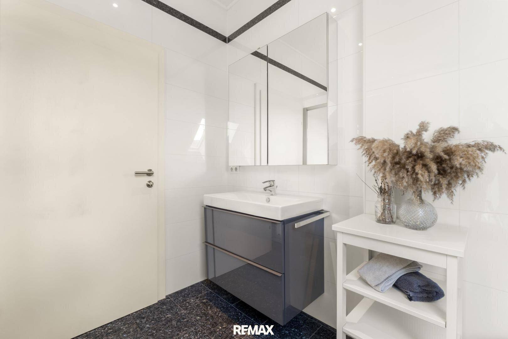 Helles Badezimmer mit modernem Waschtisch, Spiegelschrank und dunklem Fliesenboden.