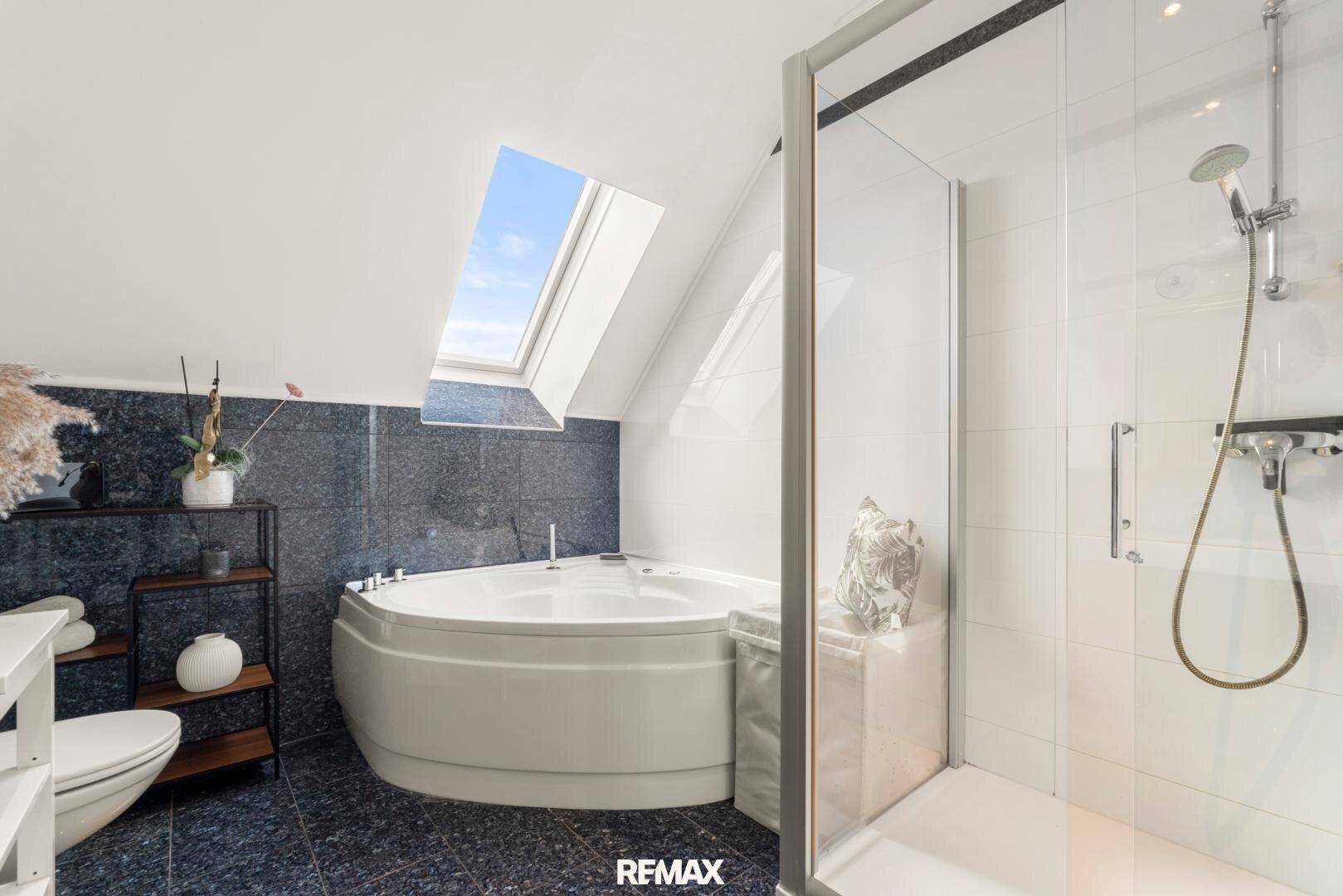 Modernes Badezimmer mit Eckbadewanne, Duschkabine, dunklen Fliesen und Dachfenster.