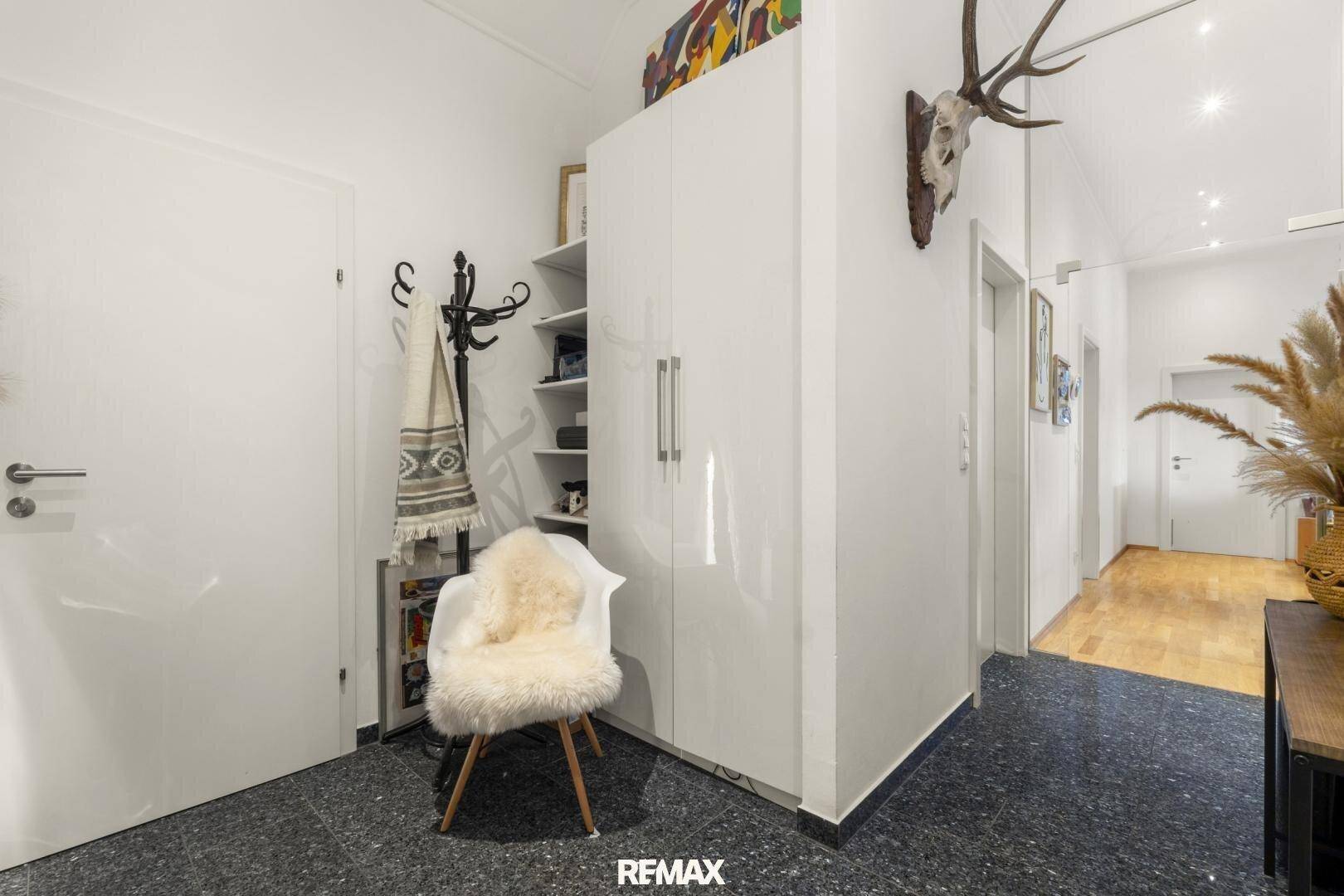 Heller Eingangsbereich mit dunklem Fliesenboden, Garderobe und Hirschgeweih-Dekoration.
