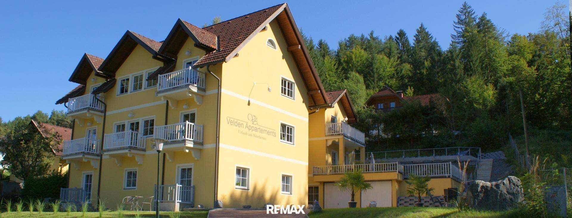 Attraktives gelbes Mehrfamilienhaus mit mehreren Balkonen, umgeben von grünen Bäumen.