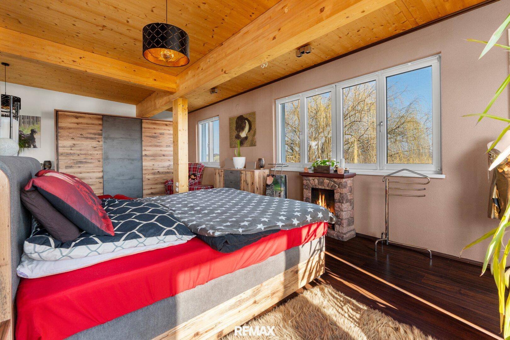 Helles Schlafzimmer mit Holzbalkendecke, Kamin und Blick ins Grüne.