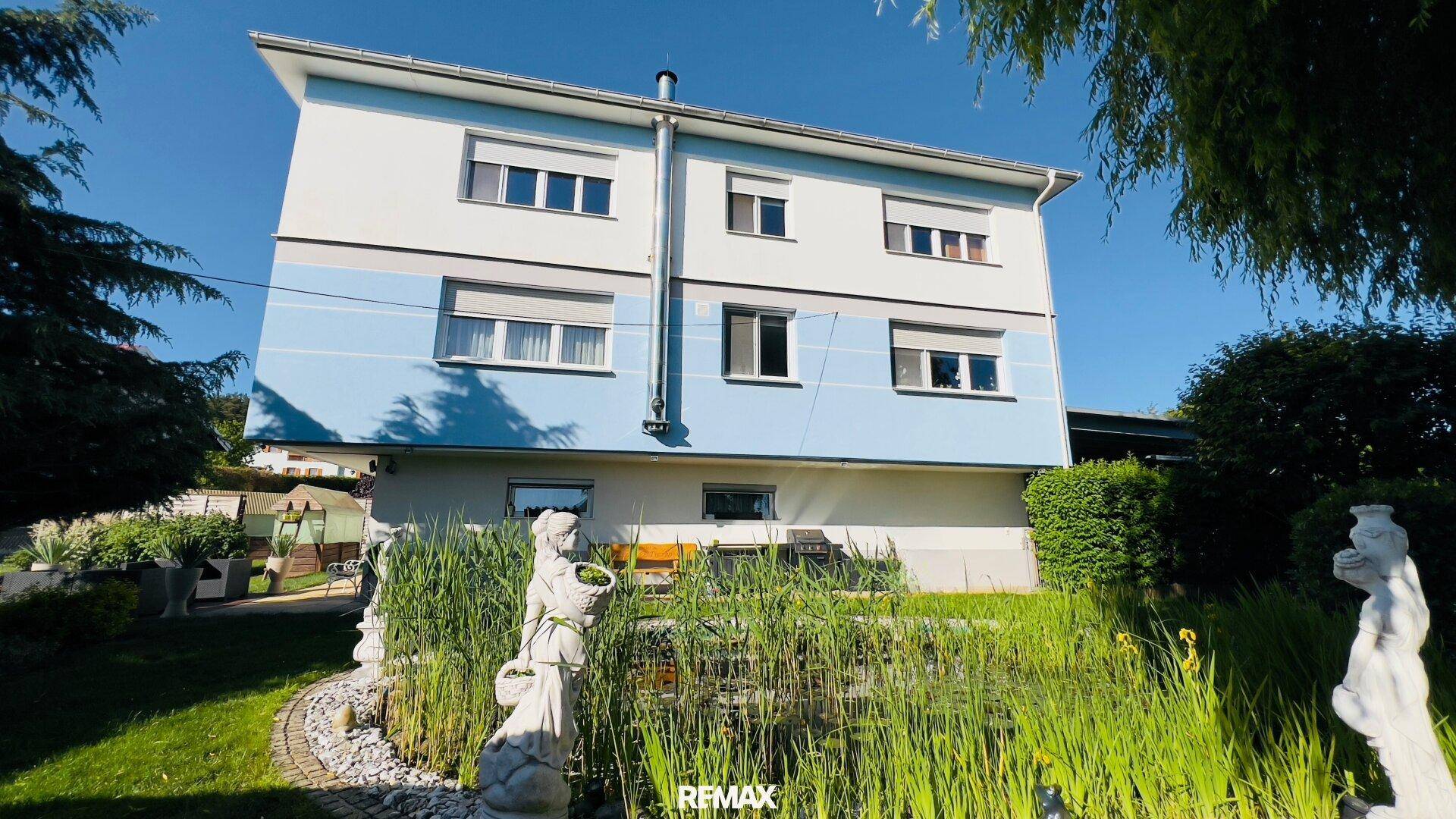 Mehrstöckiges Wohnhaus mit blauer Fassade und einem Teich im Vorgarten.