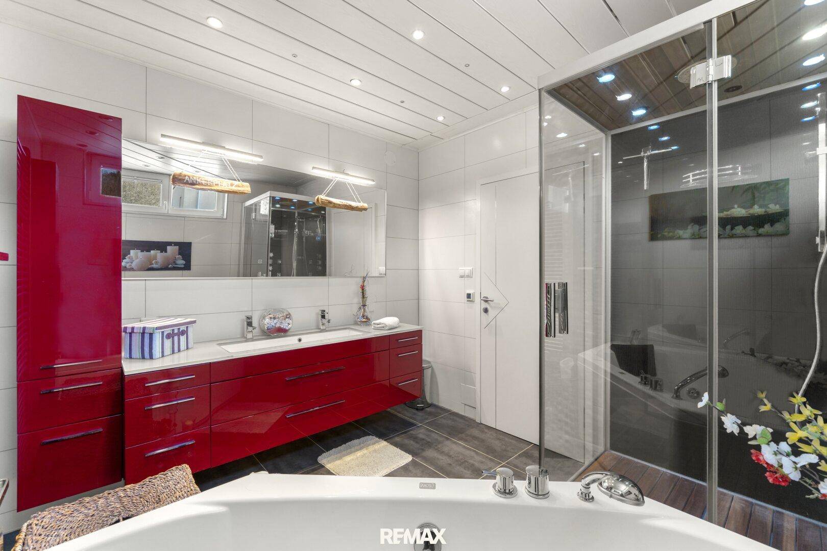 Elegantes Badezimmer mit Doppelwaschbecken, roten Schränken und großer Duschkabine.