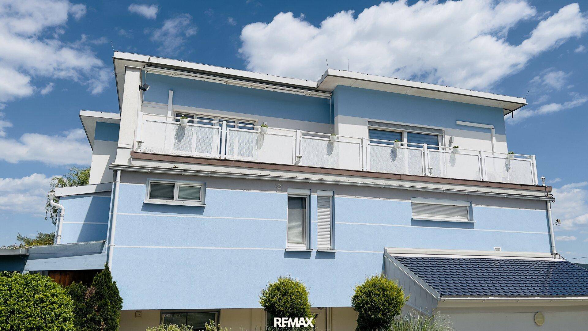 Mehrstöckiges Wohnhaus mit blauer Fassade, Balkonen und Flachdach.
