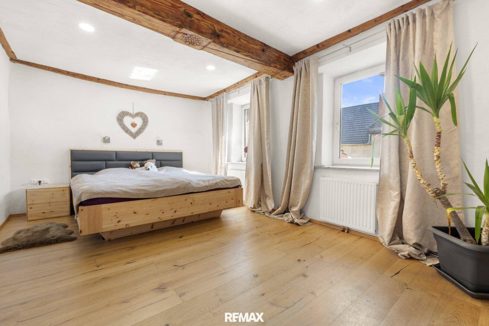 Gemütliches Schlafzimmer mit sichtbaren Holzbalken an der Decke und hellem Holzboden.