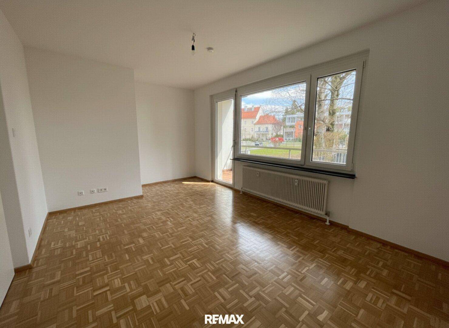 Helles Wohnzimmer mit Parkettboden, großen Fenstern und Blick auf die Umgebung.