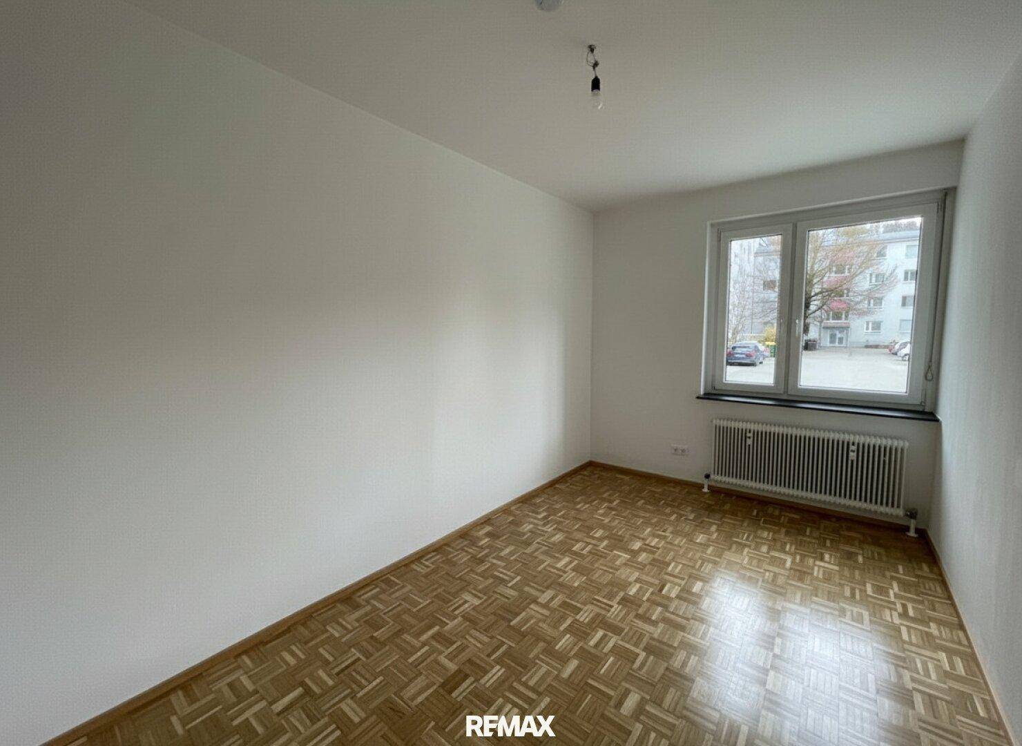 Helles Schlafzimmer mit Parkettboden, weißen Wänden und einem Fenster.