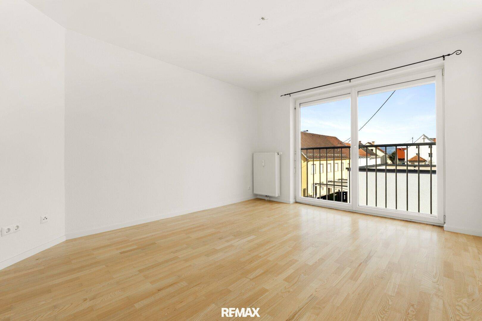 Geräumiger, heller Raum mit Holzboden und breiter Fensterfront, die viel Tageslicht hereinlässt.