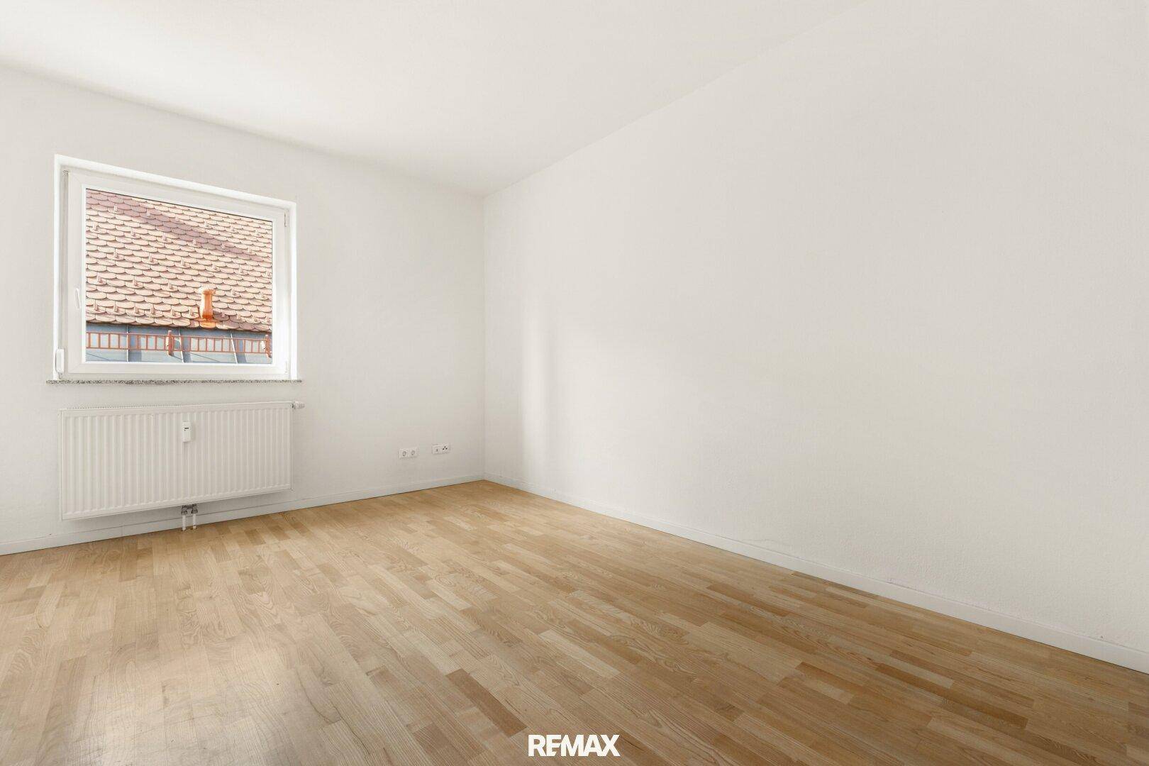 Ruhiges Schlafzimmer mit Holzboden und einem Fenster, das einen Blick auf die Dächer bietet.