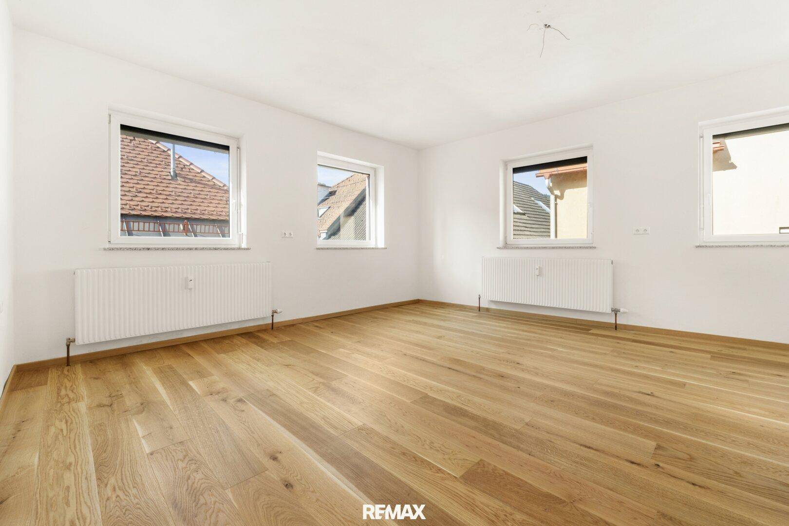 Helles Schlafzimmer mit Holzboden und drei Fenstern, die für viel Tageslicht sorgen.