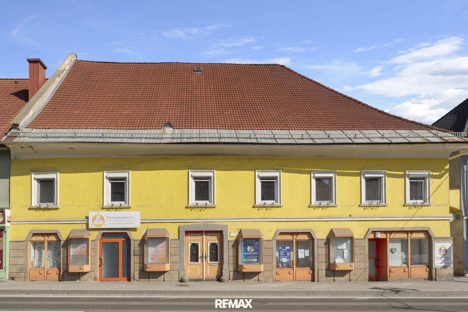Die gelbe Fassade des Gebäudes mit traditionellem Ziegeldach und mehreren Fenstern.