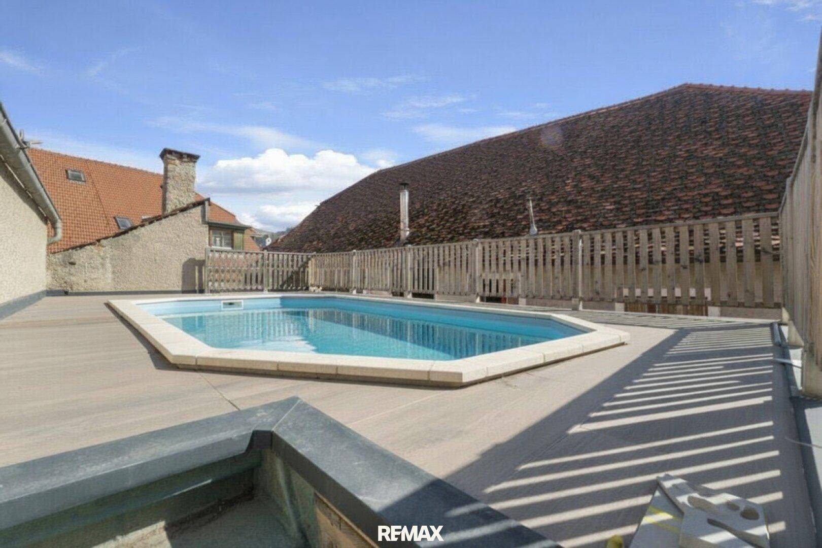 Dachpool auf einer Terrasse mit Holzzaun und Blick auf umliegende Dächer unter blauem Himmel.