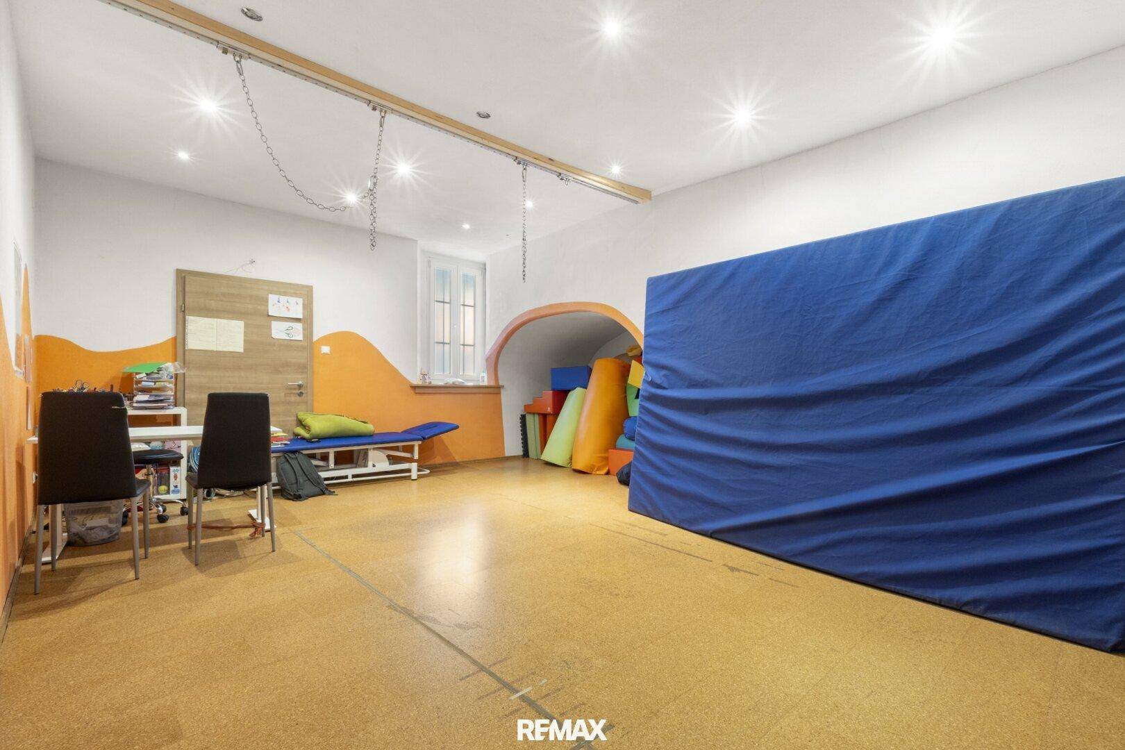 Großer Raum mit bunten Matten und Spielgeräten, ideal für Kinder oder Therapie.