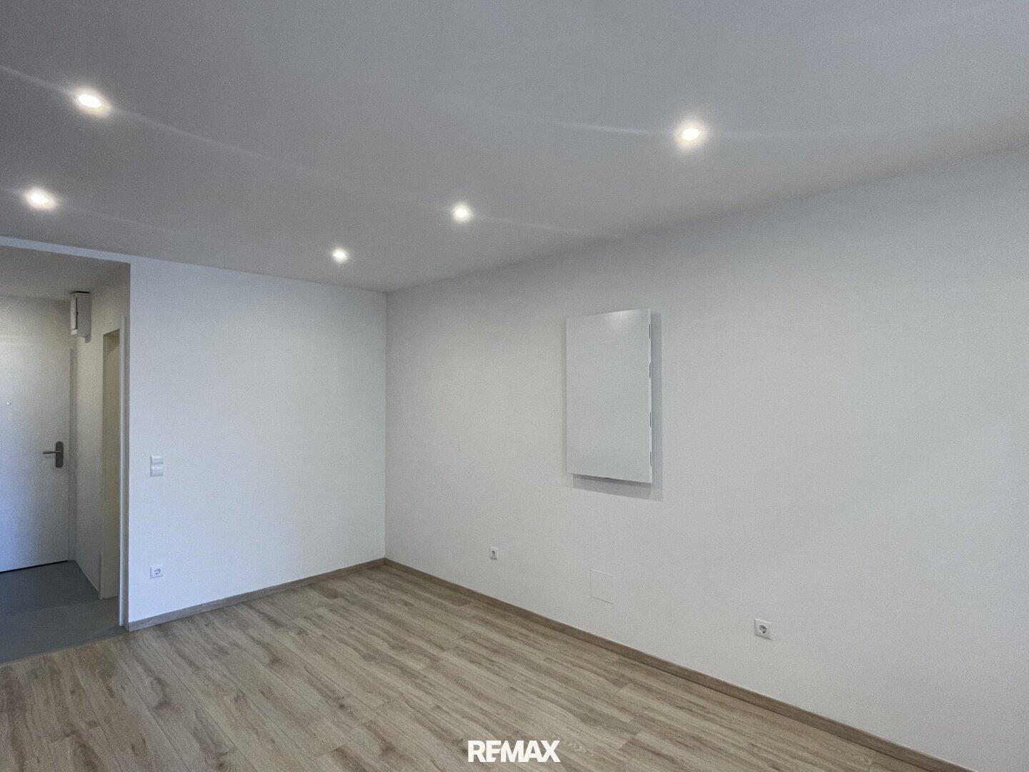 Heller Wohnbereich mit schlichten weißen Wänden und pflegeleichtem Laminatboden, ideal für moderne Einrichtung.