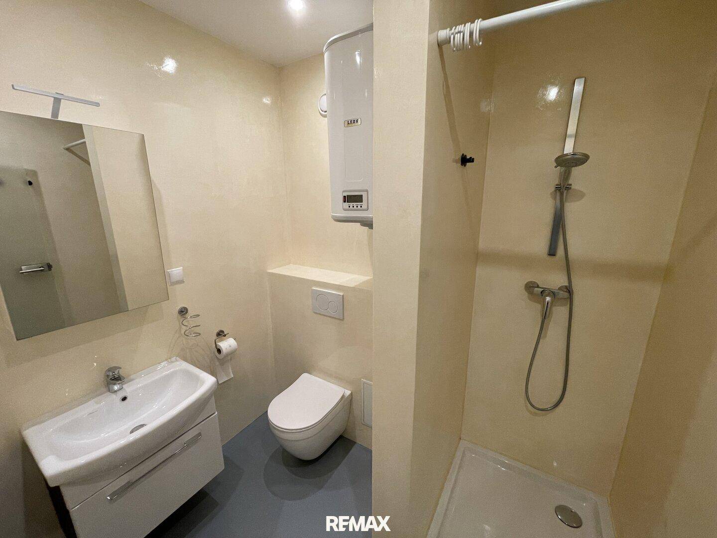 Funktionales Badezimmer mit Dusche, WC und Waschbecken, ausgestattet mit beigefarbenen Fliesen und Boiler.