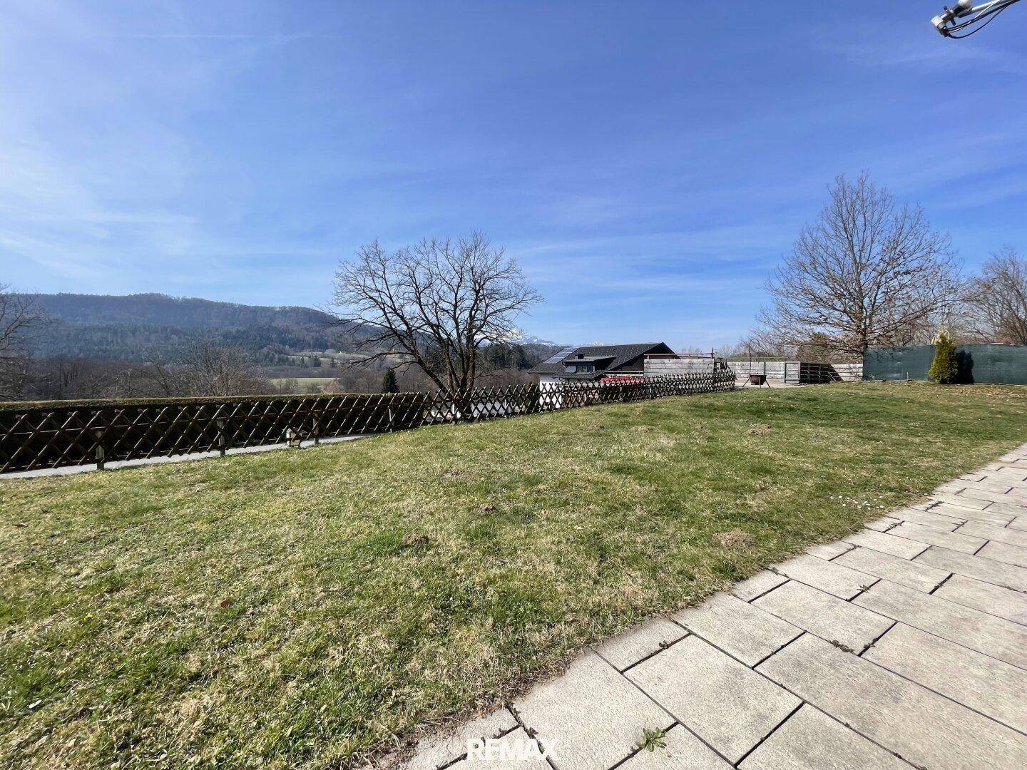 Großer Gartenbereich mit Rasenfläche, gepflastertem Weg und weitem Blick auf die grüne Landschaft.
